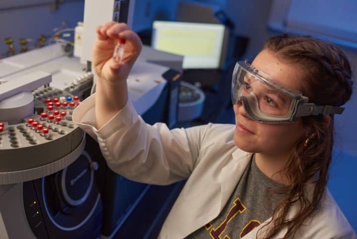 walsh university student with goggles and lab coat looking at a specimen