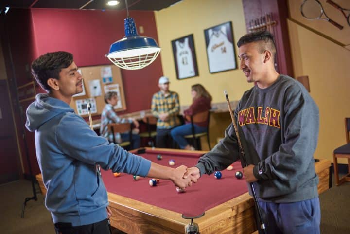 walsh university students shaking hands over a game of pool