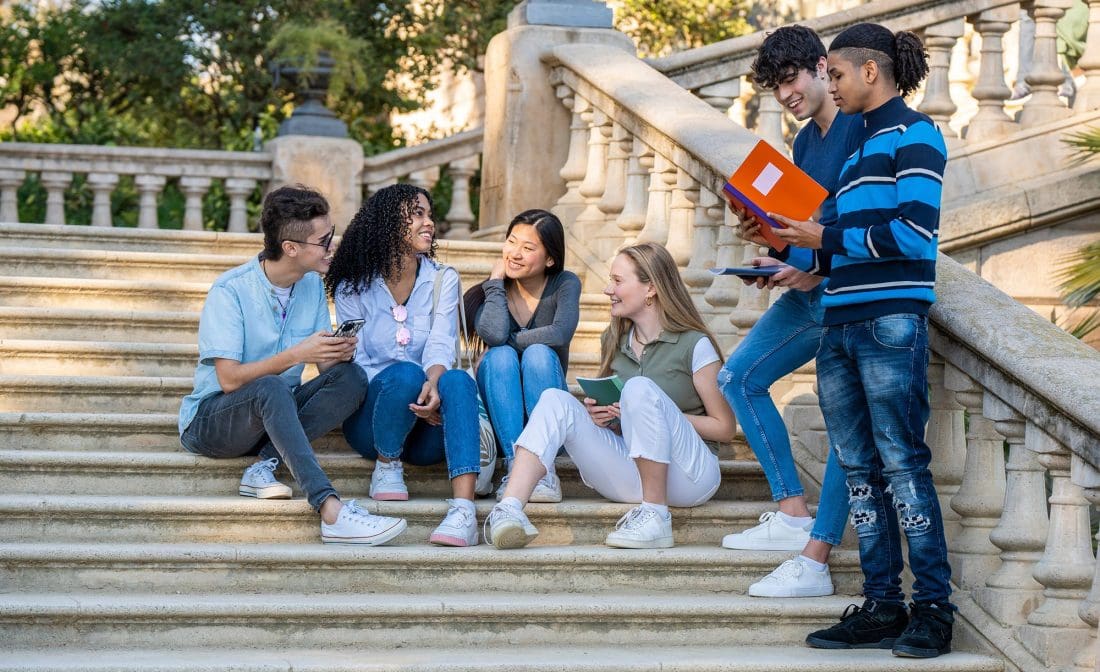 5 students sitting on stairs on college campus
