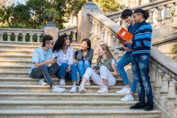 5 students sitting on stairs on college campus